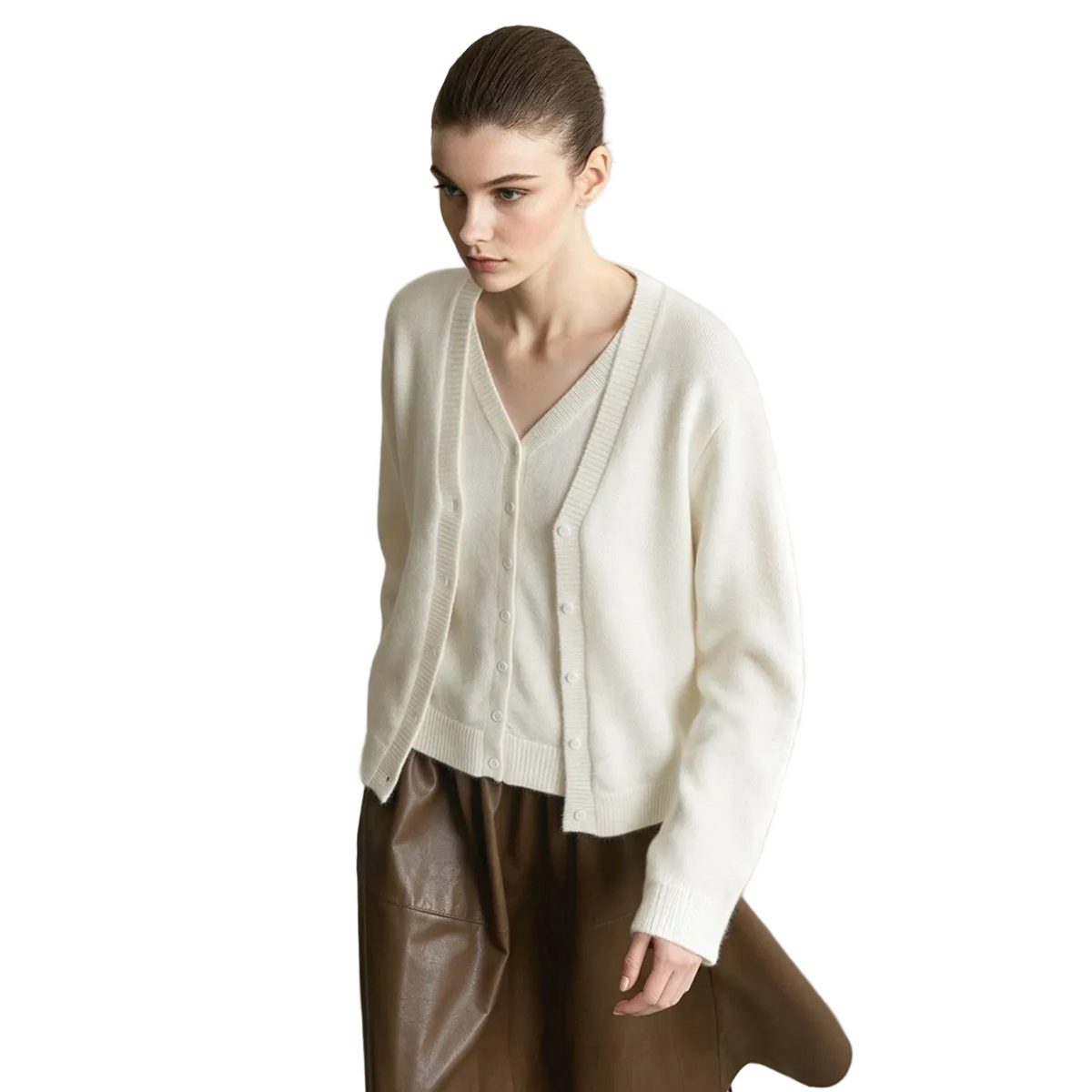 A model wearing an AMII cream-colored V-neck knit cardigan sweater and brown leather pants, standing against a minimalist light gray wall and concrete floor.
