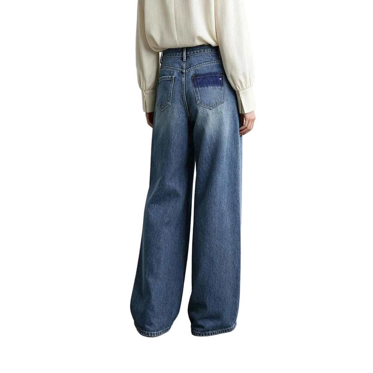 A model from behind wearing AMII wide-leg blue denim jeans with a contrasting dark blue patch pocket on the back, paired with a cream-colored blouse against a minimalist studio background.