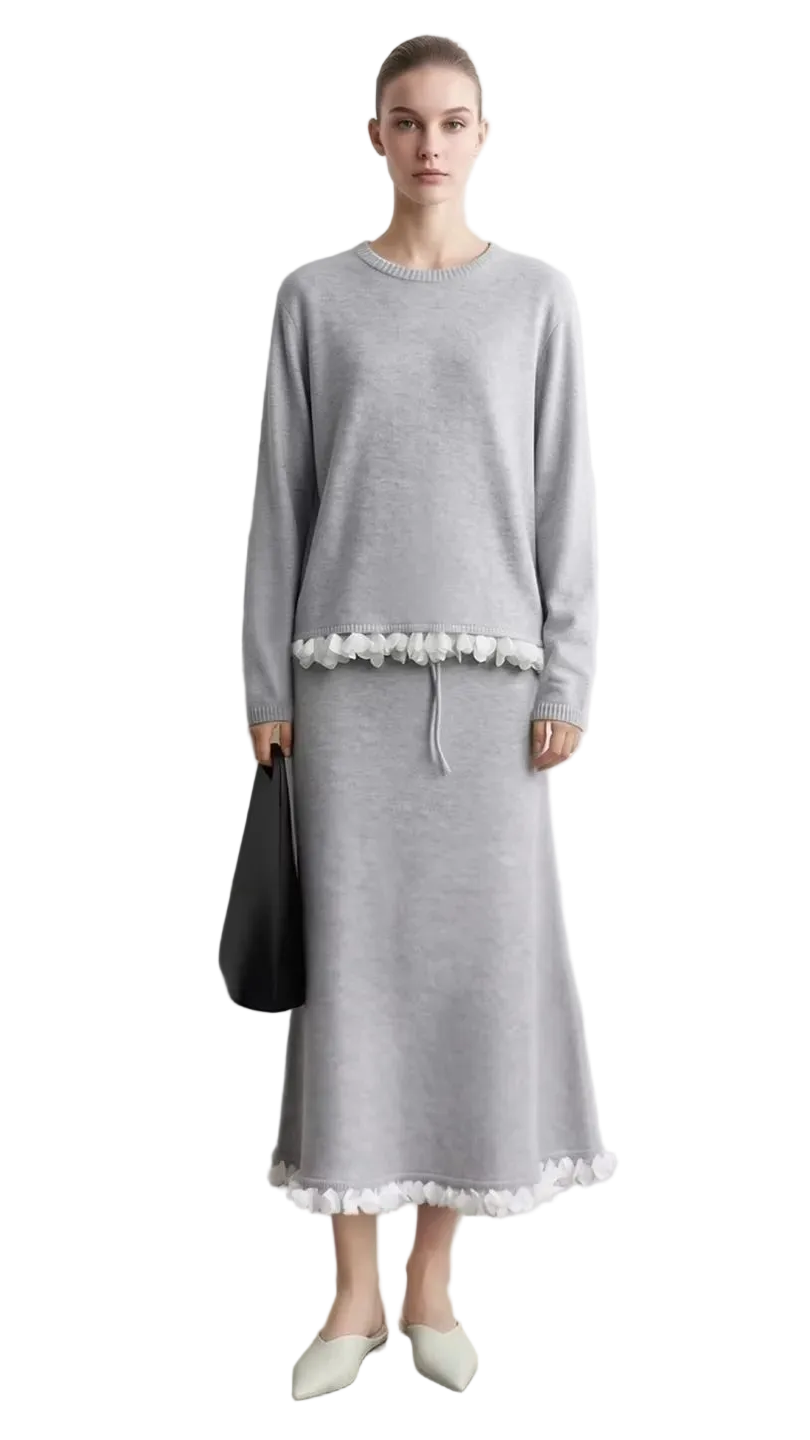 A model wears a light gray long-sleeve midi dress with white floral embroidery at the waist and hem, standing against a light gray wall. The left side of the image features a text overlay panel with the brand name 'AMII' and a close-up of the white lace embroidery.