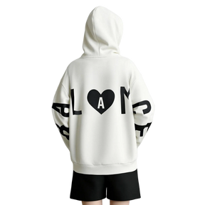 A person shown from the back wearing an oversized white hoodie with large black graphic lettering and a black heart containing the letter A on the back, paired with black shorts. The brand name AMII appears in the top left corner.