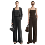 Two models wearing AMII wide-leg pants and matching tops in dark gray and dark brown, standing against a light gray wall. The left model wears a dark gray cardigan over a black tank top, and the right model wears a dark brown camisole with matching brown pants.