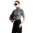 A woman modeling a fitted short-sleeve gray turtleneck sweater with black trousers and black sunglasses, holding a black handbag against a light gray studio background. The AMII brand name appears in the top left, along with a '100% sheep wool' label.