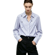 A woman wearing a light blue and white vertically striped long-sleeve button-up shirt with small embroidered floral details on the chest, paired with dark trousers. The AMII brand logo is visible in the top left corner.