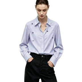 A woman wearing a light blue and white vertically striped long-sleeve button-up shirt with small embroidered floral details on the chest, paired with dark trousers. The AMII brand logo is visible in the top left corner.