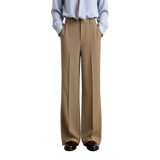 A model from the waist down wearing AMII wide-leg trousers in a light tan color, paired with a light blue button-down shirt and dark brown leather shoes, set against a plain light gray studio background.