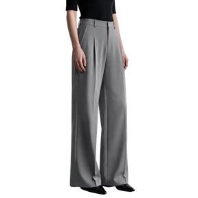 A model wearing a pair of high-waisted, wide-leg gray trousers with pleated detailing, paired with a black short-sleeve top and black pointed-toe flats. The AMII brand logo is visible in the top-left corner against a minimalist light gray studio background.