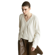 A model wearing an AMII cream-colored V-neck knit cardigan sweater and brown leather pants, standing against a minimalist light gray wall and concrete floor.