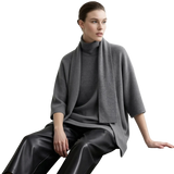 A model wearing an AMII gray knit turtleneck sweater with a draped shawl collar, paired with black leather pants, seated against a light gray background.