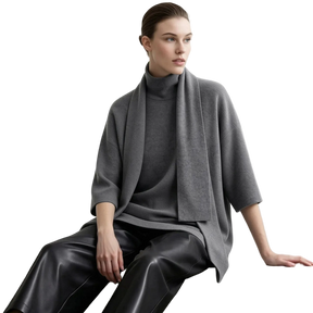 A model wearing an AMII gray knit turtleneck sweater with a draped shawl collar, paired with black leather pants, seated against a light gray background.