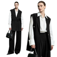 Two models wearing a black belted vest over a white long-sleeve shirt and black wide-leg trousers, standing against a light gray studio background. One model holds a black quilted handbag with a chain strap.