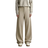 A model wearing AMII wide-leg knit trousers in a light beige color, paired with a textured beige sweater and cream shoes, standing against a neutral gray studio background.