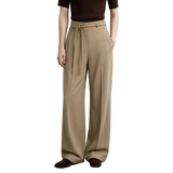 A model wearing AMII beige wide-leg pleated trousers with a drawstring waist, paired with a dark brown top and brown suede loafers, set against a minimalist studio background.