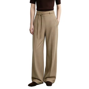 A model wearing AMII beige wide-leg pleated trousers with a drawstring waist, paired with a dark brown top and brown suede loafers, set against a minimalist studio background.