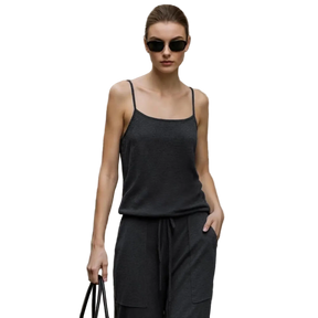 A woman wearing a dark charcoal gray sleeveless camisole top and matching drawstring pants stands outdoors against a beige stone building. The AMII brand name appears at the top left, and a product info panel on the left mentions mulberry silk and sheep wool yarn.