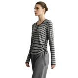 A woman modeling a long-sleeve gray and black striped knit top with a side-tie detail, paired with gray drawstring pants, against a light gray studio background. The brand name AMII is printed in the top left corner.