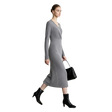 A woman models a long-sleeve gray knit midi dress with a V-neckline, paired with black ankle boots and a black handbag, set against a minimalist white studio background with the AMII logo in the top left corner.