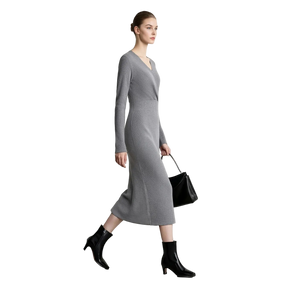 A woman models a long-sleeve gray knit midi dress with a V-neckline, paired with black ankle boots and a black handbag, set against a minimalist white studio background with the AMII logo in the top left corner.
