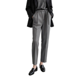 A model wearing a pair of AMII grey textured slim-fit trousers with a matching grey belt, styled with a black blazer, grey top, and black loafers against a minimalist studio background.