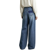 A model from behind wearing AMII wide-leg blue denim jeans with a contrasting dark blue patch pocket on the back, paired with a cream-colored blouse against a minimalist studio background.