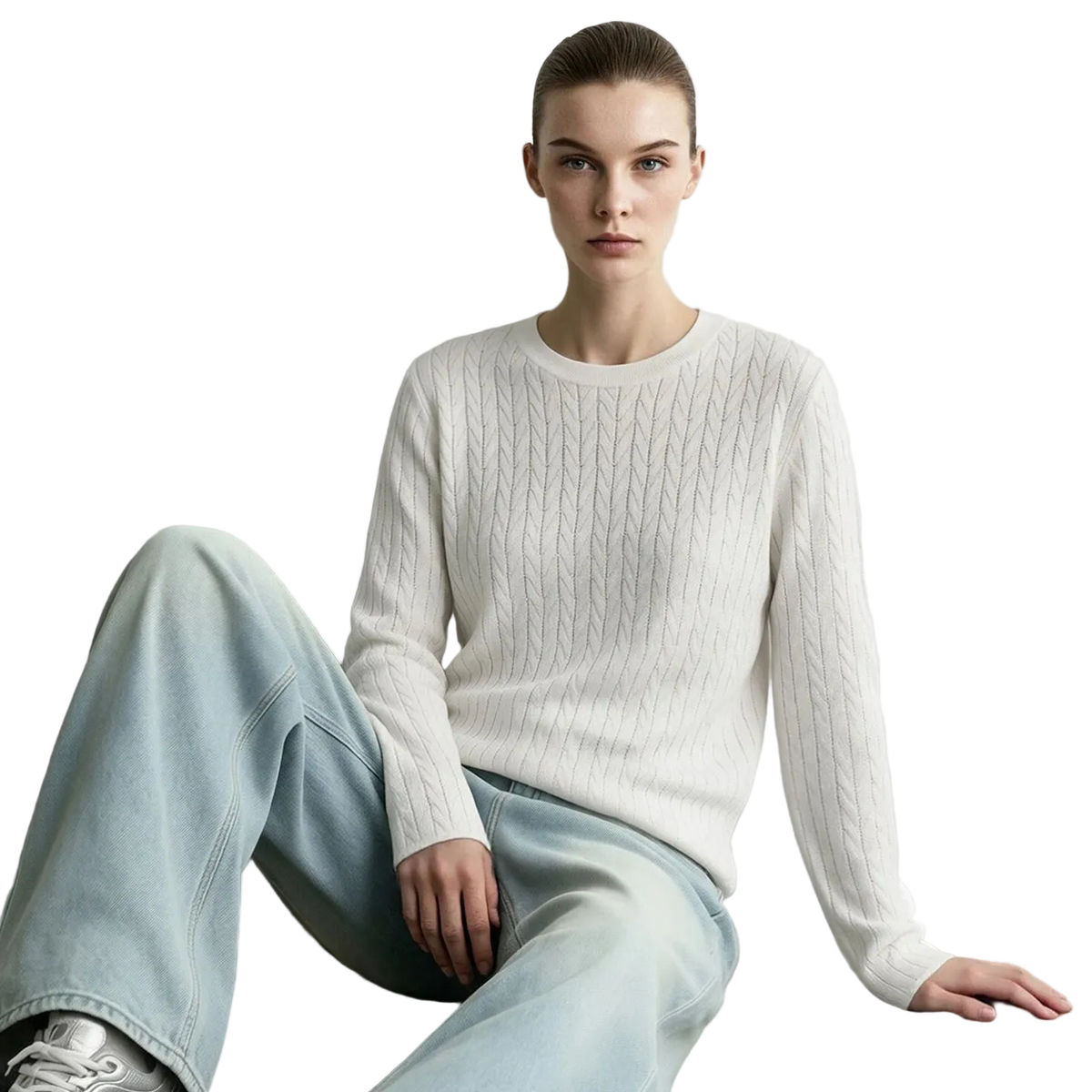 A model wearing a cream cable-knit long-sleeve sweater and light-wash wide-leg jeans, sitting against a light gray wall. The brand name 'AMII' is printed in black in the top-left corner.