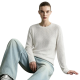 A model wearing a cream cable-knit long-sleeve sweater and light-wash wide-leg jeans, sitting against a light gray wall. The brand name 'AMII' is printed in black in the top-left corner.