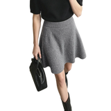 A model wearing an AMII gray knit flared skirt with a subtle glitter texture, paired with a black short-sleeve top and black boots, holding a black handbag against a minimalist studio background.