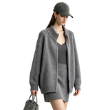 A woman modeling an AMII oversized zip-up cardigan in heather gray, paired with a matching gray knit mini skirt and a dark gray baseball cap, holding a gray handbag against a light gray studio background.