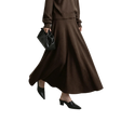 A model wearing a brown knit long-sleeve top and matching high-waisted A-line midi skirt, styled with black pointed-toe mule heels and a black leather handbag. The AMII brand logo is visible in the top left corner against a neutral gray studio background.