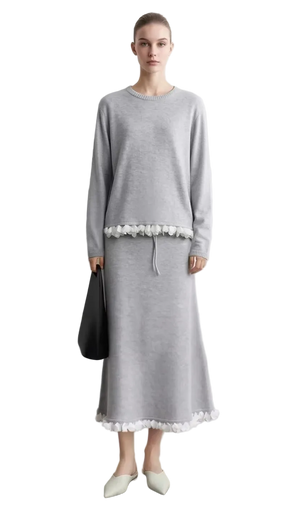 A model wears a light gray long-sleeve midi dress with white floral embroidery at the waist and hem, standing against a light gray wall. The left side of the image features a text overlay panel with the brand name 'AMII' and a close-up of the white lace embroidery.