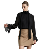 A model wearing an AMII black sheer long-sleeve blouse with a high mock neck and dramatic flared bell sleeves, paired with a beige mini skirt, against a light gray studio background.